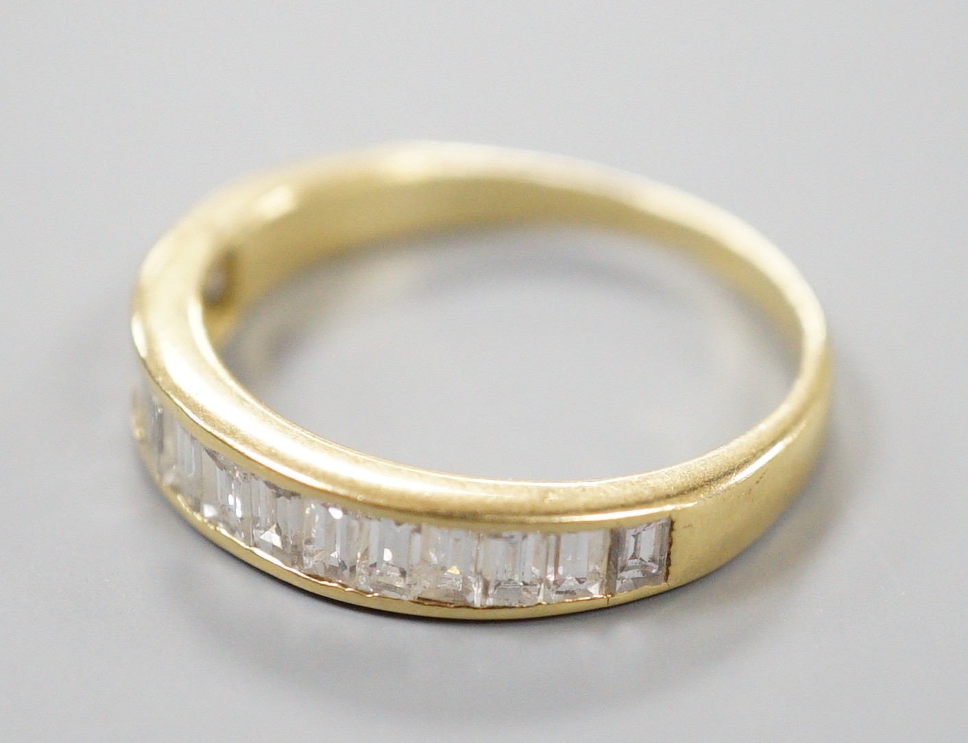A modern 18ct gold and graduated baguette cut diamond set half eternity ring, size Q, gross 3.4 grams.